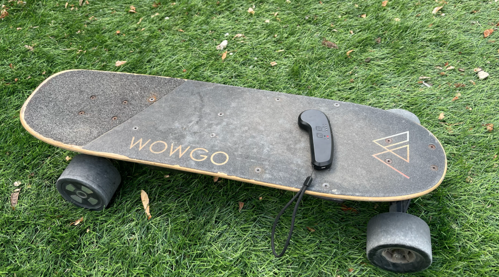 Image d'un skate électrique posé dans l'herbe de la marque wowgo avec la télécommande